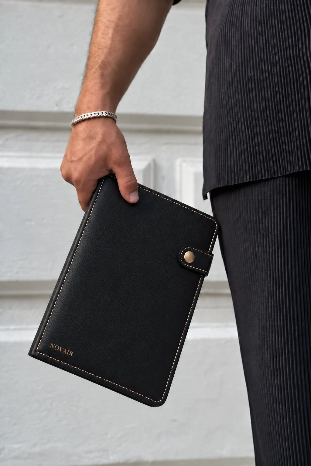 NOVAIR folio carried by the spine, beside a pleated black suit