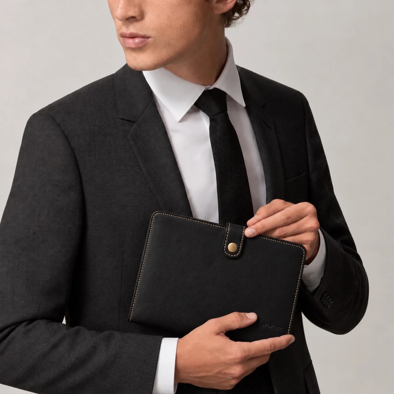 NOVAIR folio held against the chest of a man in a charcoal suit