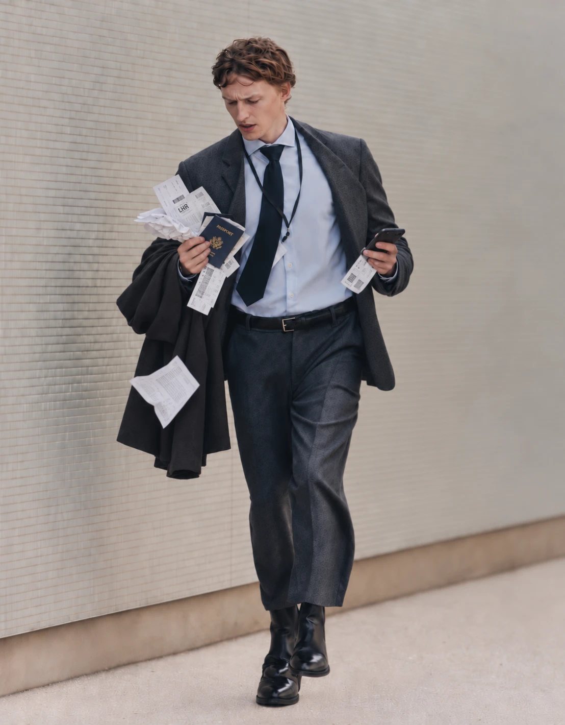 A traveller walking along a wall, passport, boarding passes and receipts spilling from one hand, phone in the other